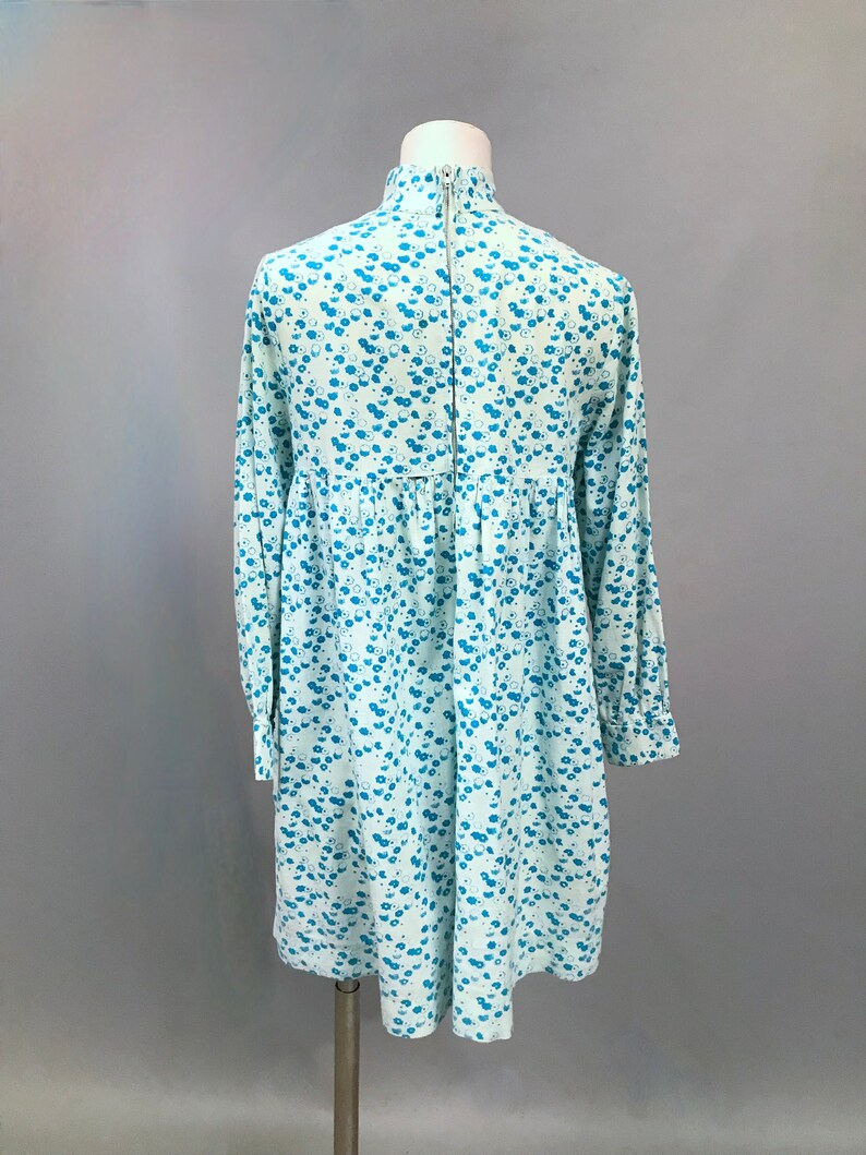May include: A light blue dress with a white floral pattern. The dress has a high neck and long sleeves. It is made of a soft, comfortable fabric and has a relaxed fit.