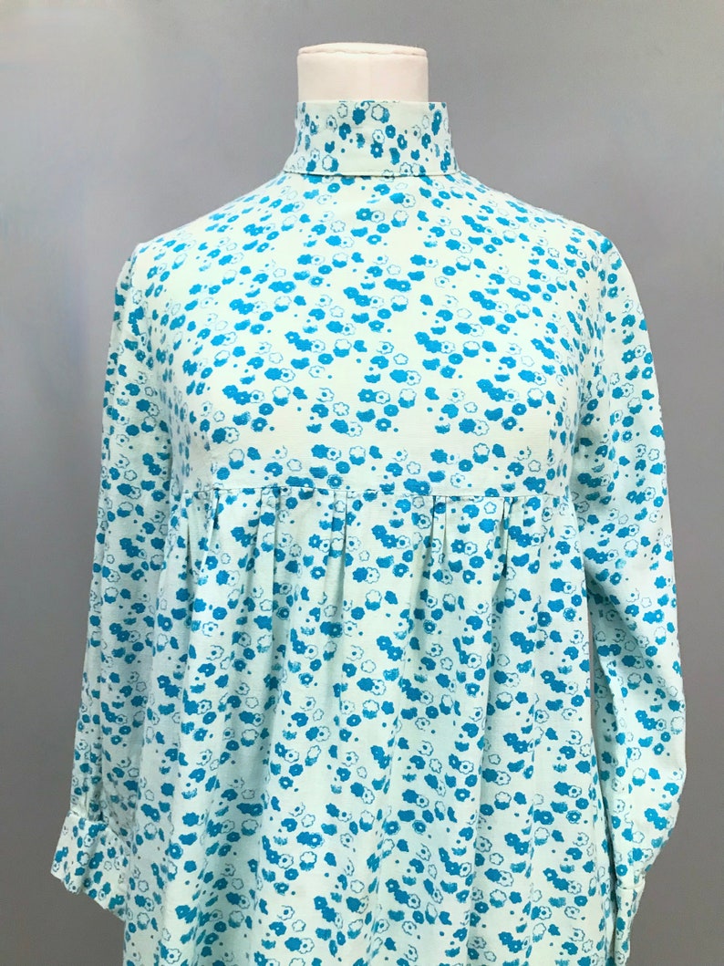 May include: A light blue dress with a high neck and long sleeves. The dress has a small blue floral pattern.