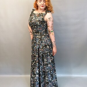 Puede incluir: Un vestido largo y fluido con estampado floral, con un corpi&ntilde;o ajustado y una falda completa. El vestido tiene un fondo azul oscuro con flores blancas y rosas. El vestido tiene un lazo en la cintura y un escote con volantes.