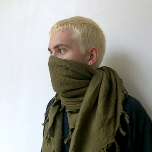 May include: A person wearing a green scarf with a textured pattern. The scarf is worn around the neck and covers the mouth and nose.