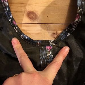 Puede incluir: Primer plano de una tela negra transparente con estampado floral. La tela tiene un estampado floral de color azul oscuro, rosa y blanco. La tela est&aacute; fruncida en la parte superior y tiene una costura alrededor del escote.