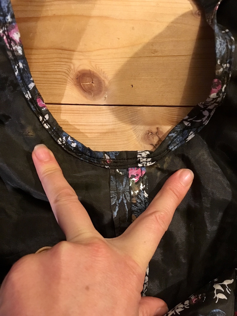 Puede incluir: Primer plano de una tela negra transparente con estampado floral. La tela tiene un estampado floral de color azul oscuro, rosa y blanco. La tela est&aacute; fruncida en la parte superior y tiene una costura alrededor del escote.