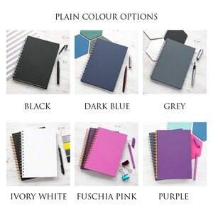 May include: Six different colored notebooks with gold spiral binding. The notebooks are arranged in two rows of three. The colors are black, dark blue, grey, ivory white, fuchsia pink, and purple.