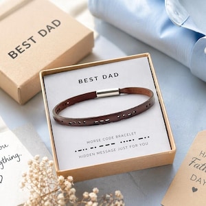 Puede incluir: Una pulsera de cuero marrón con código Morse en una caja de regalo con la inscripción "BEST DAD". La caja también contiene una tarjeta con el mensaje "HIDDEN MESSAGE JUST FOR YOU". Una etiqueta de "Happy Father's Day" y una tarjeta que dice "Thank you for everything" también son visibles.