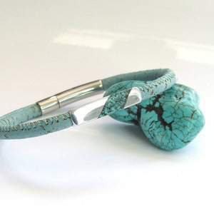 Peut inclure: Un bracelet en cuir bleu clair avec une fermeture en m&eacute;tal argent&eacute;. Le bracelet est en li&egrave;ge et a une surface textur&eacute;e.