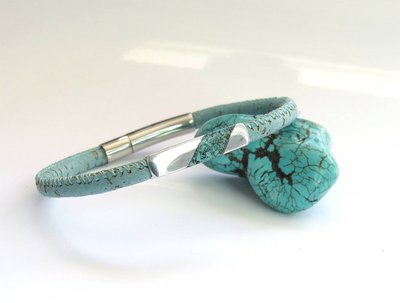 Peut inclure: Un bracelet en cuir bleu clair avec une fermeture en m&eacute;tal argent&eacute;. Le bracelet est en li&egrave;ge et a une surface textur&eacute;e.