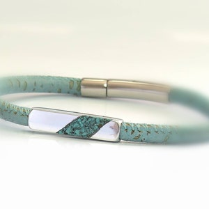Peut inclure: Un bracelet en cuir turquoise avec un fermoir en argent en forme de barre. La barre est incrust&eacute;e de turquoise.