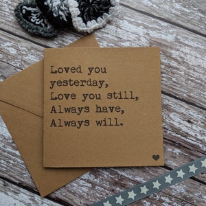 Puede incluir: Una tarjeta marr&oacute;n con el texto "Loved you yesterday, Love you still, Always have, Always will." La tarjeta est&aacute; sobre una superficie de madera con una cinta gris con estrellas blancas y tres corazones de ganchillo en blanco y negro.