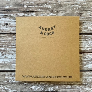 Puede incluir: Una tarjeta de papel marr&oacute;n con el texto "Audrey & Coco" en un c&iacute;rculo negro con las palabras "Spread the Love" debajo. La parte inferior de la tarjeta tiene la direcci&oacute;n del sitio web "www.audreyandcoco.co.uk" impresa en negro.