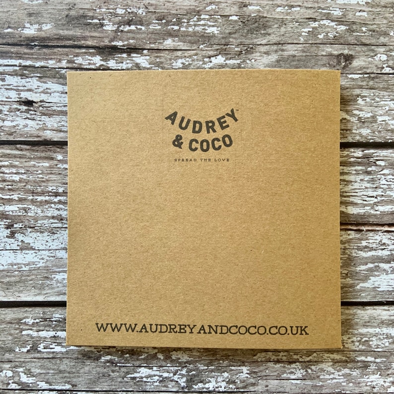 Puede incluir: Una tarjeta de papel marr&oacute;n con el texto "Audrey & Coco" en un c&iacute;rculo negro con las palabras "Spread the Love" debajo. La parte inferior de la tarjeta tiene la direcci&oacute;n del sitio web "www.audreyandcoco.co.uk" impresa en negro.