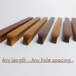 Könnte beinhalten: Holzschrankgriffe in verschiedenen Brauntönen, horizontal angeordnet. Jeder Griff hat einen gebogenen Griff und einen rechteckigen Körper. Der Text "Any length . Any hole spacing." ist darunter abgebildet.