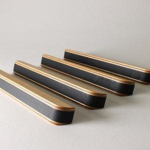 May include: Four wooden cabinet pulls with a black center stripe and natural wood edges. The pulls are rectangular with rounded ends, and are arranged diagonally across the frame.