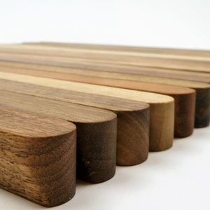 Könnte beinhalten: Eine Nahaufnahme eines Schneidebretts aus Holz, das aus verschiedenen Holzarten besteht. Das Brett besteht aus langen, dünnen Holzstreifen, die in einem versetzten Muster angeordnet sind. Das Holz ist eine Mischung aus hell- und dunkelbraunen Farben.