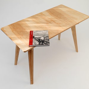 May include: A light wood table with a book titled "Edvard Munch The Scream" on top. The table has four legs that are angled outwards.