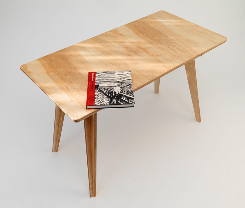 May include: A light wood table with a book titled "Edvard Munch The Scream" on top. The table has four legs that are angled outwards.
