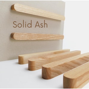 Könnte beinhalten: Rechteckige Holzstäbe mit abgerundeten Kanten, einige an einer hellen Oberfläche befestigt. Der Text "Solid Ash" ist auf der Oberfläche sichtbar. Die Stäbe sind aus hellfarbigem Holz.