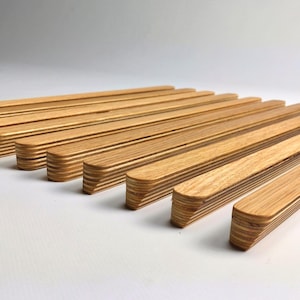 May include: Ten wooden drawer pulls with a natural wood finish. The pulls are made of layered wood and have a rounded edge.