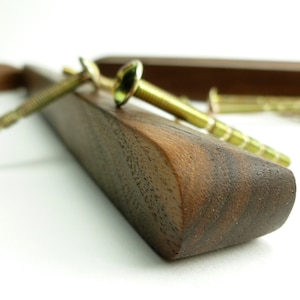 Könnte beinhalten: Nahaufnahme einer dunkelbraunen Holzschubladen-Griff mit zwei goldenen Schrauben. Der Schubladen-Griff ist glatt und hat eine abgerundete Kante.