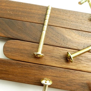 Könnte beinhalten: Vier goldene Schrauben mit flachen Köpfen und Schlitzantrieb liegen auf einer Holzoberfläche. Das Holz ist dunkelbraun und hat eine Maserung.