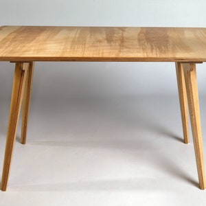 May include: A simple wooden table with a light wood top and four legs. The legs are angled and made of the same wood as the top.