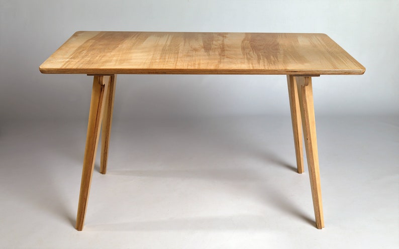 May include: A simple wooden table with a light wood top and four legs. The legs are angled and made of the same wood as the top.