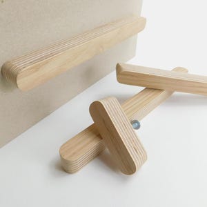 Könnte beinhalten: Drei Holzknaufgriffe mit natürlicher Oberfläche und einem gestreiften Muster. Die Griffe sind aus Sperrholz und haben eine rechteckige Form.