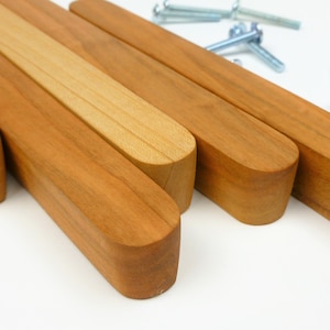 May include: Four wooden drawer pulls with rounded edges and a natural wood finish. The pulls are arranged in a staggered pattern, with the top pull slightly offset from the others.