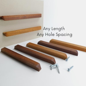 May include: Six wooden cabinet pulls in various lengths and shades of brown. The pulls have a rectangular shape and are made of solid wood. The pulls are arranged in a staggered pattern on a white surface. Any Length Any Hole Spacing.