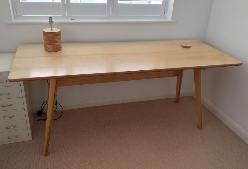 May include: A light wood desk with a simple design. The desk has a rectangular top and four legs. The desk is made of light wood and has a natural finish.