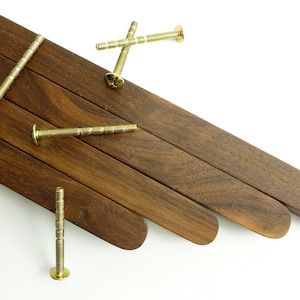 Peut inclure: Vue en angle de plusieurs lattes de bois brun foncé aux extrémités arrondies, et plusieurs vis dorées éparpillées sur la surface. Les vis ont une tête plate et une tige filetée. Le grain du bois est visible.