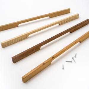 以下が含まれることがあります： さまざまな茶色とタンの色合いの木製キャビネットプルが4つあり、くぼんだハンドルデザインになっています。小さな銀色のネジがいくつか近くに散らばっています。プルは家具やキャビネット用である可能性があります。