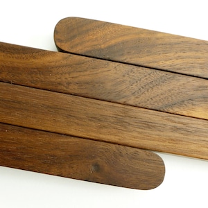 May include: Close-up of several wooden serving utensils. The utensils are a rich, dark brown colour with rounded ends. The wood grain is visible, adding texture to the smooth surface. The items are arranged diagonally against a white background.