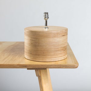 Puede incluir: Una l&aacute;mpara de mesa de madera con un acabado de madera natural y una pantalla de metal plateado. La l&aacute;mpara est&aacute; sobre una mesa de madera.