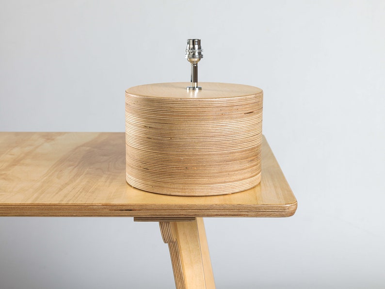 Puede incluir: Una l&aacute;mpara de mesa de madera con un acabado de madera natural y una pantalla de metal plateado. La l&aacute;mpara est&aacute; sobre una mesa de madera.