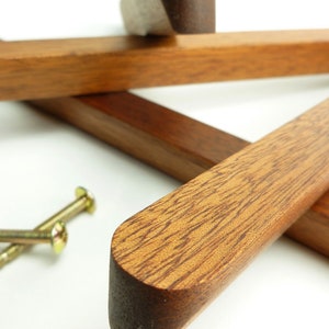 Könnte beinhalten: Nahaufnahme von Holzkomponenten, möglicherweise für Möbel oder ein Bastelprojekt. Das Holz hat einen satten, warmen Braunton mit sichtbarer Maserung. Zwei goldfarbene Schrauben sind ebenfalls vorhanden, was auf eine Montage oder Konstruktion hindeutet. Die Komponenten sind auf einer weißen Oberfläche angeordnet.