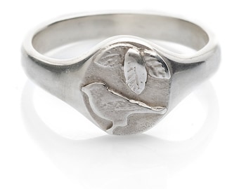 May include: A silver ring with a bird and leaves design. The ring is oval shaped and has a textured finish.