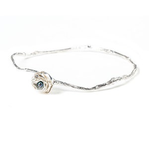 May include: A silver bangle bracelet with a delicate, textured design. The bracelet features a single, small, iridescent pearl set in a silver flower.
