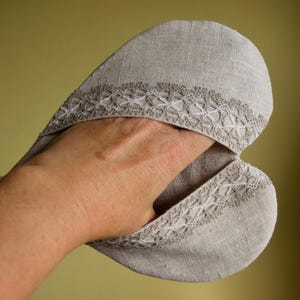May include: A heart-shaped oven mitt made of light gray linen. The mitt features a decorative white lace trim along the edges and a loop for hanging. The mitt is designed to protect hands from heat.