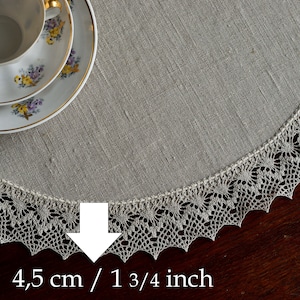 May include: A round, off-white linen table runner with a delicate crocheted lace border. The lace border is 1 3/4 inches wide.