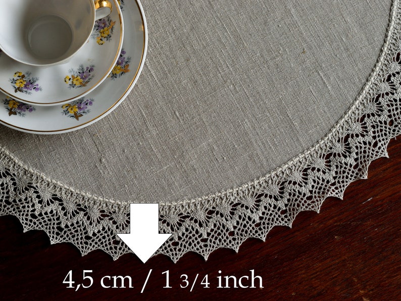May include: A round, off-white linen table runner with a delicate crocheted lace border. The lace border is 1 3/4 inches wide.