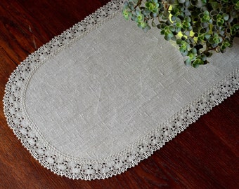 Puede incluir: Un camino de mesa ovalado de color gris claro con un borde de encaje blanco. El camino de mesa está hecho de lino y tiene una textura sutil.
