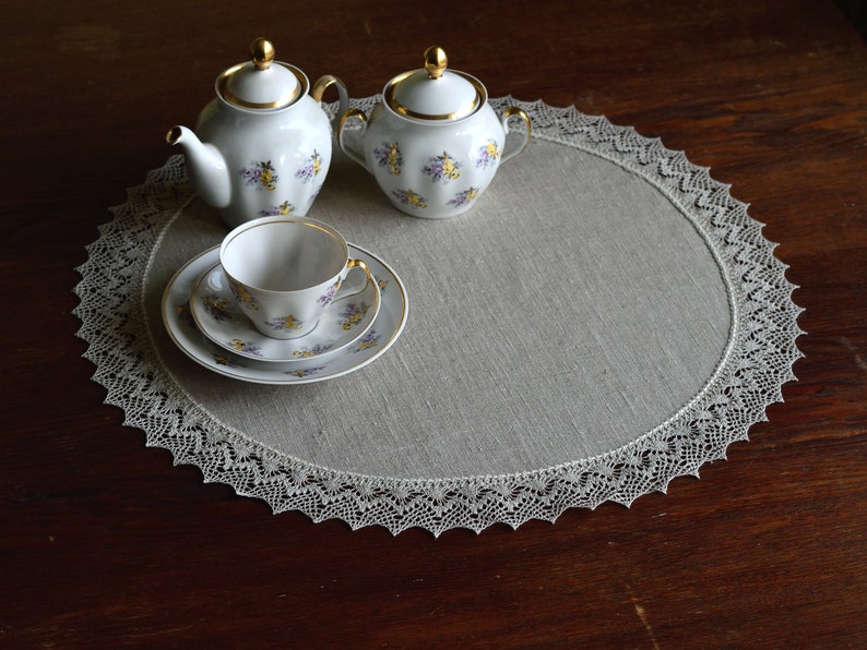 May include: A white tea set with floral designs on a linen table runner with a lace border.