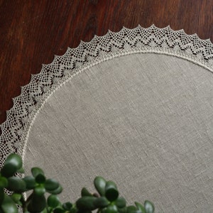 May include: A round, beige linen placemat with a delicate white crocheted lace border.