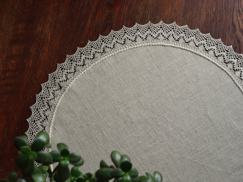 May include: A round, beige linen placemat with a delicate white crocheted lace border.