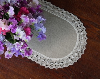 May include: A white oval table runner with a delicate lace border. The runner is made of linen and has a subtle texture. A bouquet of purple, pink, and white sweet peas sits on top of the runner.