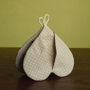 Può includere: Una teiera in tessuto beige a pois bianchi. La teiera ha un design unico a forma di petalo e un manico ad anello in corda. La teiera è realizzata in un tessuto morbido ed è progettata per mantenere il tè caldo.