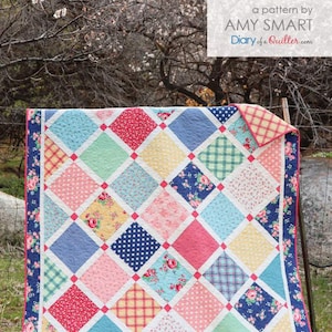 May include: A quilt with a lattice pattern in shades of blue, pink, yellow, and green. The quilt is made up of squares with different floral and geometric prints. The quilt is hanging on a fence with a sign that reads "Lattice, a pattern by Amy Smart, Diary of a Quilter.com".