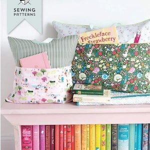 May include: A pink bench displays colorful books and patterned reading pillows. One pillow has a pink and white village print, another has a floral design. A book titled "Freckleface Strawberry" rests on top. The image includes a sewing pattern logo.