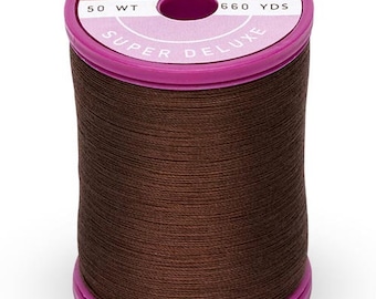 Puede incluir: Una bobina de hilo de algodón y acero marrón, etiquetada "Cotton + Steel Super Deluxe 50 Wt 660 Yds"