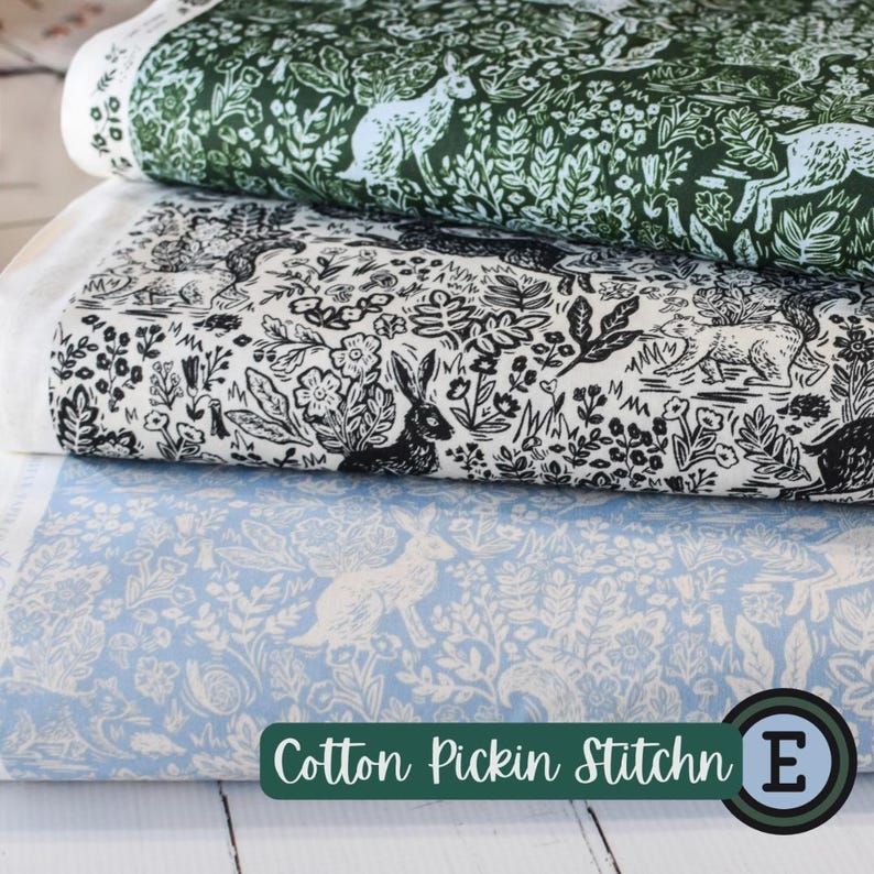 May include: Three stacked fabric rolls with nature-themed patterns. The top roll features a dark green design with white rabbits and foliage. The middle roll has a black and white illustration of rabbits and flowers. The bottom roll is light blue with white rabbits and floral elements. The text "Cotton Pickin Stitchn" is visible.